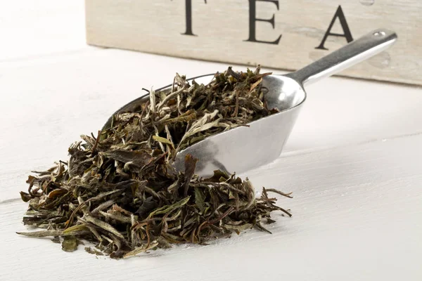 Сухе, сире листя білого чаю в металевій сопілці на білому дерев'яному столі — стокове фото