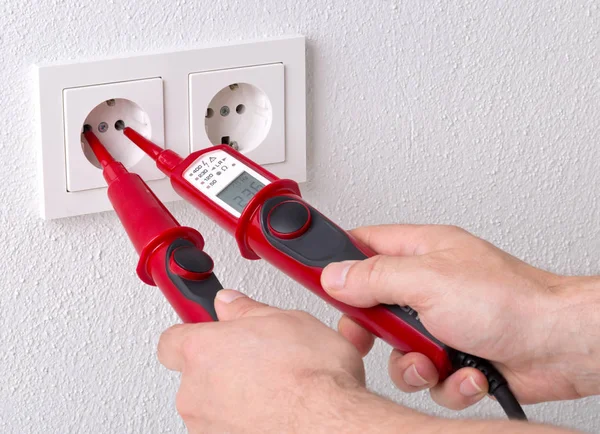 Male electrician measuring power on wall outlet with measuring d — Stock Photo, Image