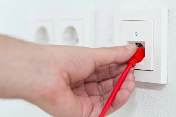 El hombre enchufa el cable de red rojo en la toma de pared para oficina o privada — Foto de Stock