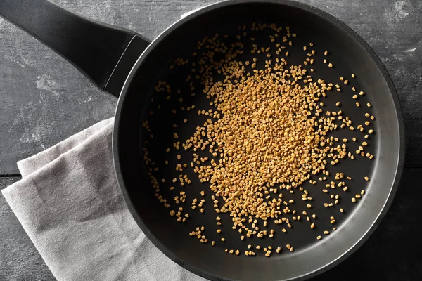 Сушене, сире насіння пажитника в залізній сковороді для обсмажування на темному настрої — стокове фото