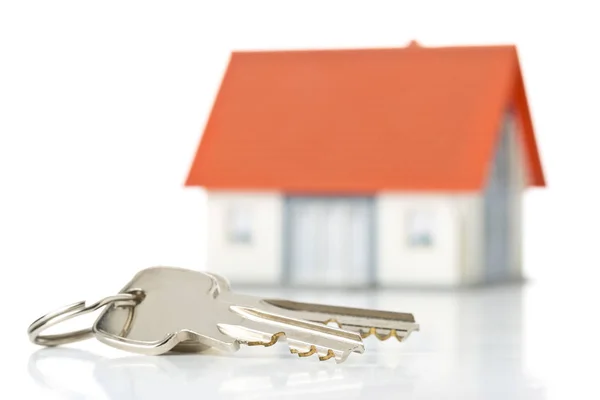 Klíče domu před modelovým domem přes bílou pozadí-domů — Stock fotografie