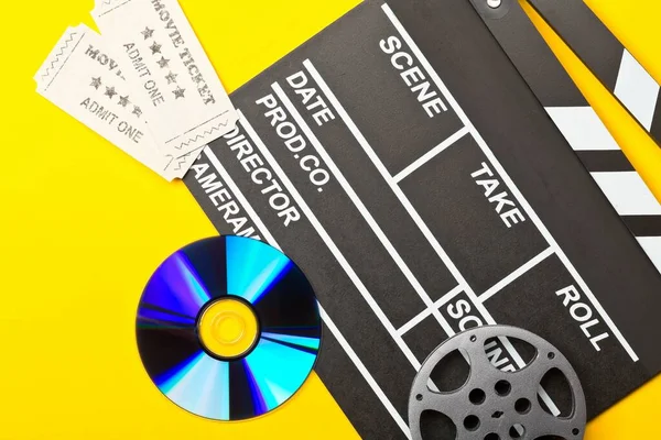 Single, black, open movie clapper or clapper-board with dvd movie disc, film reel and movie theatre tickets flat lay top view from above on yellow or orange background - digital movie, home cinema or movie night concept