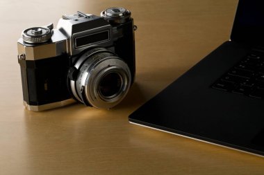 Ofisteki ahşap masada dizüstü bilgisayarın yanında bulunan analog SLR kamera, dijital fotoğrafçılık veya resim işleme konsepti, seçici odaklanma