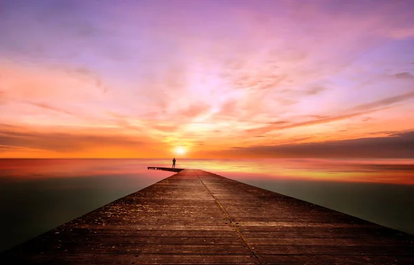 Een persoon op een pier observeert en overweegt een prachtige zonsondergang Stockfoto