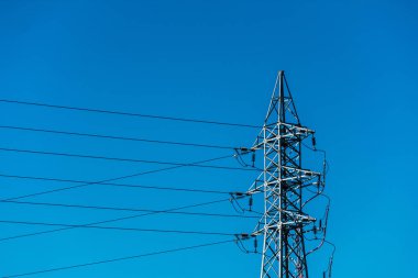 Mavi gökyüzünde kabloları olan yüksek voltajlı elektrik kulesi.