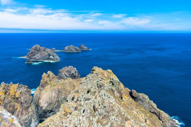 Mavi suyu ve güneşli gökyüzü ile okyanustaki kayalık.