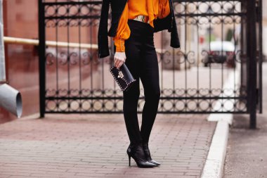 Sokak, ofis, parlak stil. Genç kadın, iş tarzı, siyah ceket, siyah pantolon, siyah çanta, güneş gözlüğü, turuncu gömlek, kemer, bilezik. Ayrıntılar.
