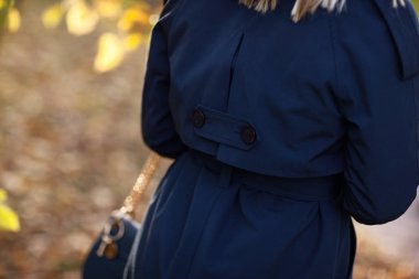 Güzel moda kadın ellerinde sonbahar mavi ceket parkta bir çanta ile size yürür. Ayrıntılar