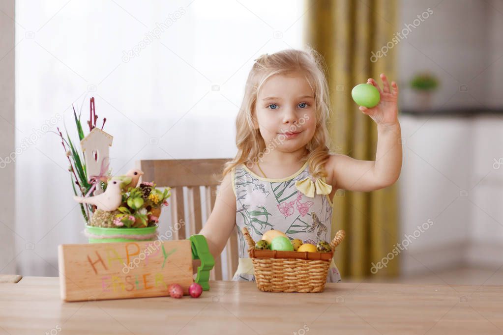 The child sits at the holiday table with a basket of Easter eggs. Holds an egg in his hand and considers
