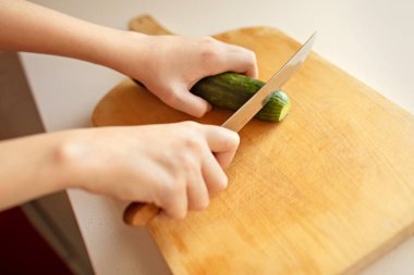 Kız salatalık ahşap bir gemide keser. Portre, mutfak, eller, k