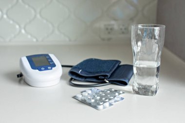 Elektronik tonometer, hapları ve bir bardak su üzerinde beyaz bir tabl