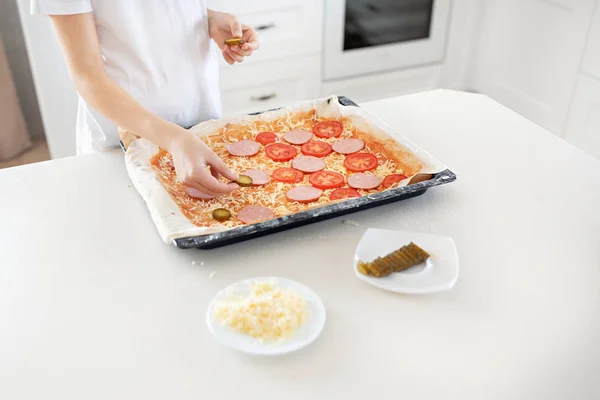A child makes a pizza. Salami, cheese, ketchup, tomatoes, cucumb