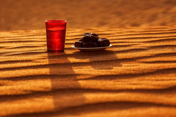 Ramadan Kareem. Na pozadí nádherného slunce západu slunce v poušti se nachází sklenice vody a data v talíři — Stock fotografie