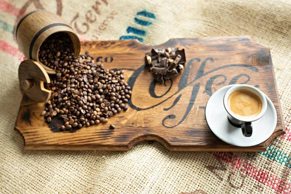 Chicchi di caffè sparsi, una tazza di caffè espresso, pezzi di cioccolato con noci su una tavola di legno . — Foto Stock