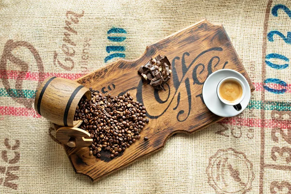 Кофейные зерна, чашка эспрессо, кусочки шоколада с орехами на деревянной доске . — стоковое фото