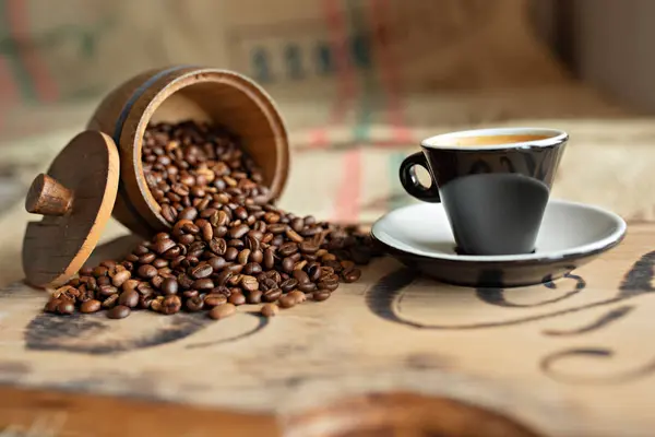 Grãos de café espalhados, uma xícara de café expresso, pedaços de chocolate com nozes em uma tábua de madeira . — Fotografia de Stock