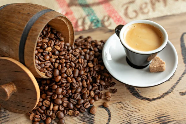 Grãos de café espalhados, uma xícara de café expresso, pedaços de chocolate com nozes em uma tábua de madeira . — Fotografia de Stock