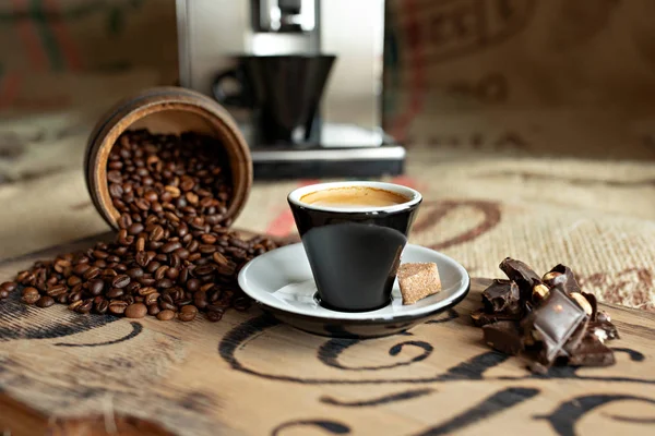 Grãos de café espalhados, uma xícara de café expresso, pedaços de chocolate com nozes em uma tábua de madeira . — Fotografia de Stock