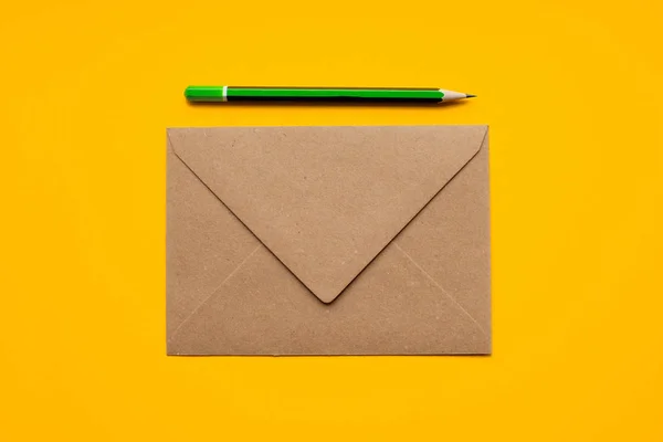Brauner Umschlag und einfacher grüner Bleistift auf gelbem Hintergrund, Draufsicht. — Stockfoto