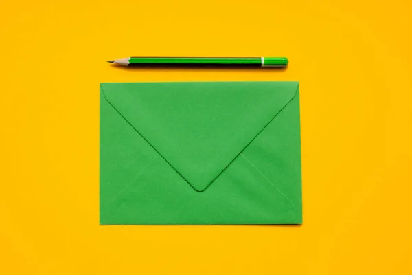 Grüner Umschlag und einfacher grüner Bleistift auf gelbem Hintergrund, Draufsicht — Stockfoto