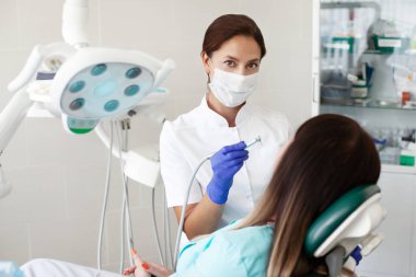 Kadın diş hekimi bir hastayı tedavi eder. Maskeli bir kadın klinikte diş sandalyesinde oturuyor. Tıp, sağlık, diş hekimliği kavramı.