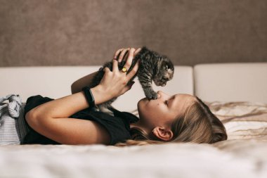 Çocuk yatakta yatıyor ve İngiliz küçük bir kedi yavrusu ile oynuyor