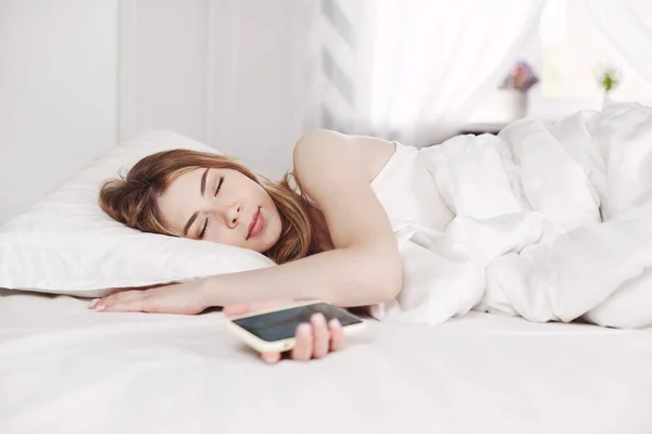 Ένα Νεαρό Όμορφο Κορίτσι Άσπρες Πιτζάμες Κοιμάται Κρατώντας Ένα Τηλέφωνο — Φωτογραφία Αρχείου