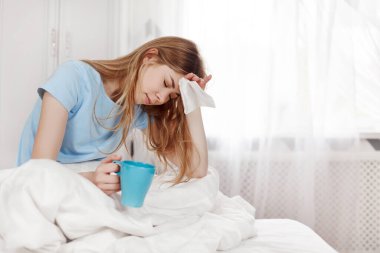 Başı ağrıyan hasta bir kız yatak odasındaki battaniyenin altında elinde kağıt mendille sıcak çay içiyor. Mevsimsel hastalıklar, grip, alerjiler. Metin için boşluk