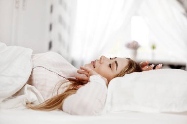 Genç, gülümseyen güzel bir kız yatak odasında yatıyor. Kız sabah uyandıktan sonra esniyor. Yan görünüm, metin için boşluk