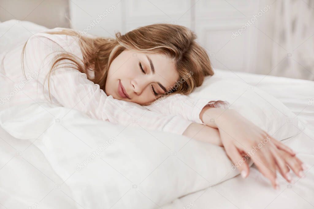 A beautiful girl is sleeping on a bed in her bedroom at home in the early morning. Concept of recreation and healthy lifestyle