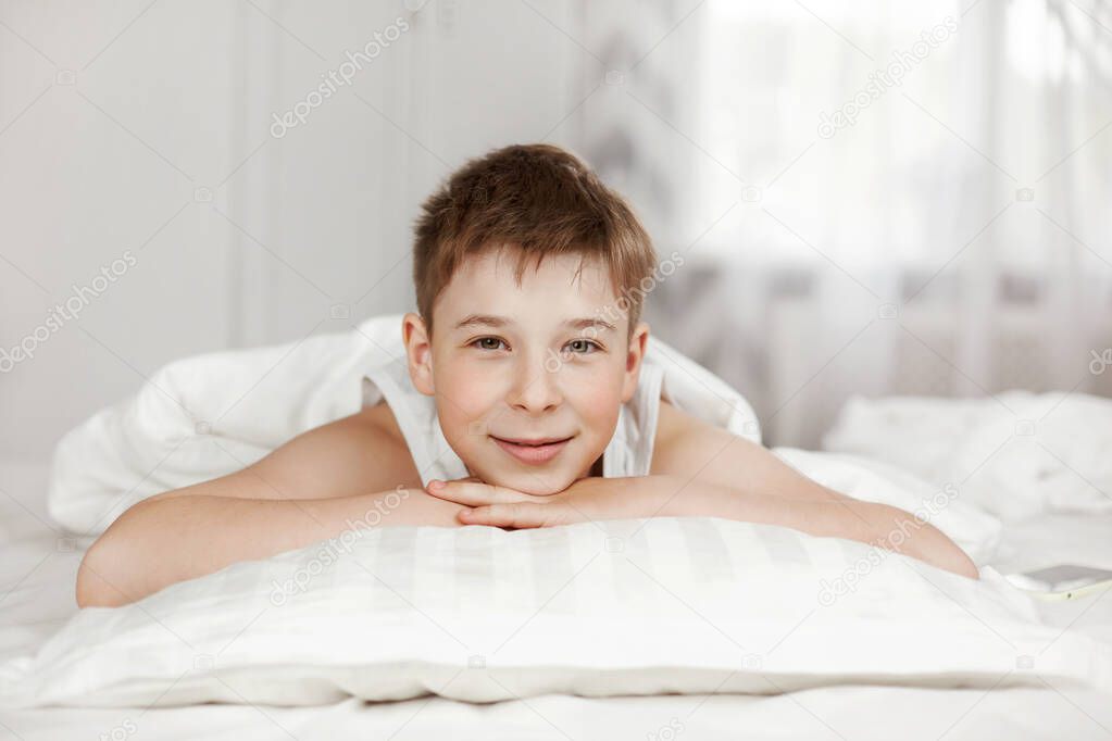 A cute teenage boy is lying on the bed in the bedroom and smiling. Close-up, space for text