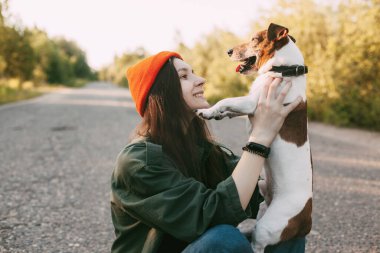 Güzel bir esmer, köpeğini kollarına alıp gülümsüyor. Kız evcil hayvanıyla birlikte doğada dinleniyor. Arkadaşlık ve özen kavramı