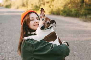 Güzel bir esmer, köpeğini kollarına alıp gülümsüyor. Kız evcil hayvanıyla birlikte doğada dinleniyor. Arkadaşlık ve ilgi kavramı. Bulanık arkaplan, metin için boşluk