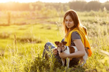 Güzel bir genç kız çimlerin üzerinde oturuyor ve köpeğine sarılıyor. Bir kız ve evcil hayvanı doğa yürüyüşünden sonra dinleniyorlar. Arkadaş, Dostluk, Bakım. Metin için boşluk