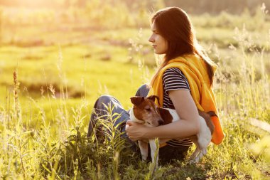 Güzel bir genç kız çimlerin üzerinde oturuyor ve köpeğine sarılıyor. Bir kız ve evcil hayvanı doğa yürüyüşünden sonra dinleniyorlar. Arkadaş, Dostluk, Bakım. Yan görünüm, metin için boşluk