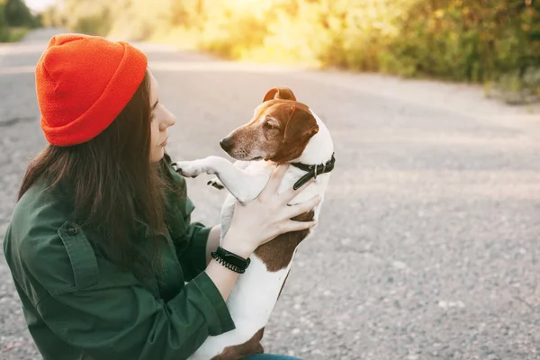 オレンジの帽子の美しい女の子は彼女の腕の中で彼女の犬を保持します 少女はペットの世話をし 新鮮な空気の中で彼と歩く ペット — ストック写真