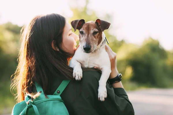 肩に緑のリュックを背負ったジャケットの少女が腕に犬を抱えて抱きかかえている 少女はペットと一緒に歩く リアビュー テキストの場所 — ストック写真