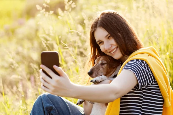 An attractive teen girl takes photos of herself and her dog using a mobile phone camera. A girl takes a photo while walking with her pet