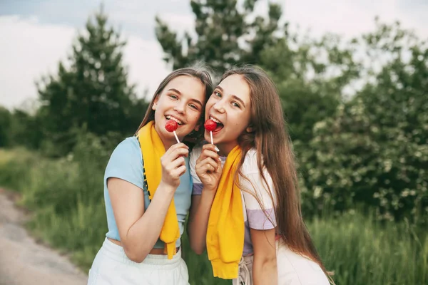 Δύο Χαρούμενα Έφηβα Κορίτσια Κρατώντας Ένα Φωτεινό Κόκκινο Γλειφιτζούρι Καραμέλα — Φωτογραφία Αρχείου
