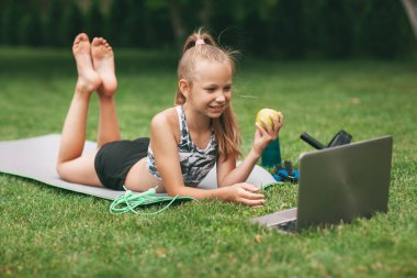 Genç bir kız evinin yanında online eğitim aldıktan sonra elinde bir elma ve muz tutuyor. Spor haberleri. Sağlıklı yaşam tarzı