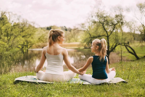 Anne ve kızı bahçede Lotus pozisyonunda oturuyorlar. Aile dışarıda yoga pratiği yapıyor. Arka plan, metin için boşluk