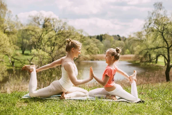 Güzel bir genç kadın ve kızı sağlıklı bir yaşam tarzını sürdürürken spor kıyafetleriyle yoga yapıyorlar.