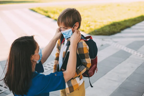 Mom puts a child a mask and escorts to school or kindergarten. A boy with a masked backpack during a coronavirus.