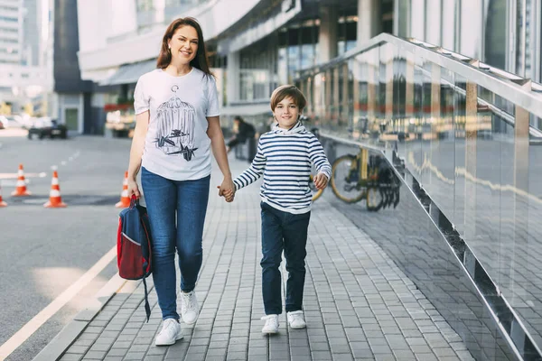 Anne bir elinde sırt çantası taşır, diğer elinde de oğlunu tutar. Neşeli, güler yüzlü bir çocuk annesiyle birlikte okuldan mesajlaşmak için uzaklaşıyor.