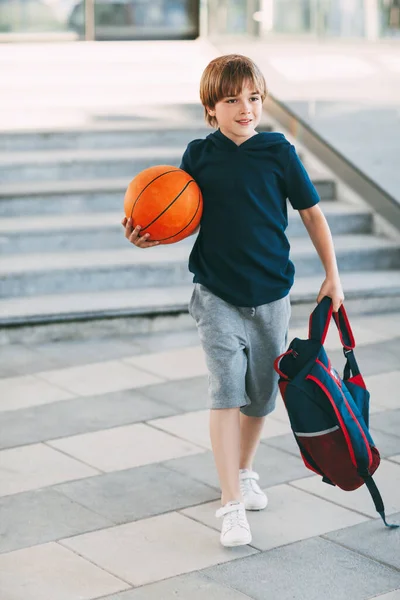 손에는 가방을 손에는 농구공을 귀여운 소년은 몸매가 운동을 싶지만 농구를 — 스톡 사진