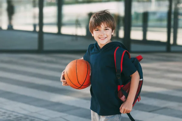 Spor üniformalı, sırt çantası ve basketbol topuyla güzel bir çocuğun portresi. Çocuk gülümsüyor ve topu elinde tutuyor. Eğitim, eğitim