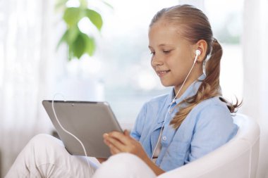 Kulaklıklı bir öğrenci elinde tabletle bir sandalyeye oturur ve online ders sırasında ödevini yapar. Çevrimiçi eğitim, internetten öğrenme. yakın plan