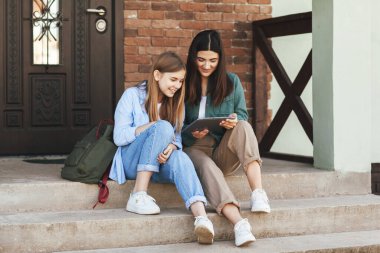 Evin yakınındaki basamaklarda, üniversiteden gelen iki güzel kız-kız kardeş oturuyor, bir tablet kullanıyor ve gülüyorlar. Teknoloji, eğitim