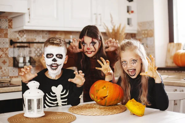Gelukkig kinderen vieren Halloween in de keuken thuis in kostuums en make-up met pompoen lantaarn Jack kijken naar de camera en glimlachen. — Stockfoto