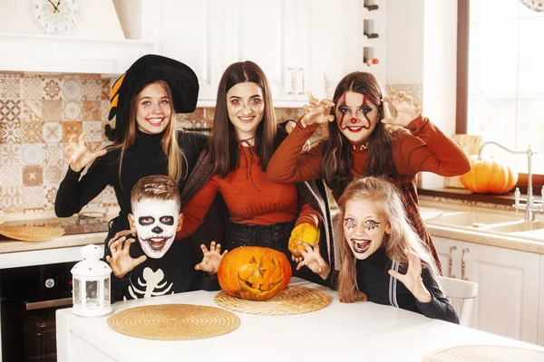 Happy kids świętować halloween w kuchni w domu w kostiumach i makijażu z dyni latarnia Jack patrząc w aparat i uśmiech — Zdjęcie stockowe